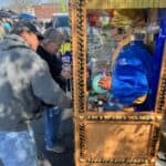 Two people interact with a fortune-telling machine featuring a life-size animatronic figure dressed in blue inside a glass booth at an outdoor market, where party rentals Long Island, NY and bounce house Long Island options are available nearby.