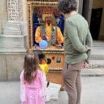 A man and two young children stand in front of a Zoltar fortune teller machine outside a stone building with ornate carvings. The kids, dressed in colorful costumes, look ready for fun—perfect for a day of party rentals Long Island style.
