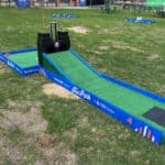 A mini golf hole with a green turf ramp leads up to a black castle. Blue borders labeled "The Park" and "UBS Arena" surround hole 4, set outdoors on grass—perfect for party rentals Long Island, NY alongside bounce house Long Island fun.