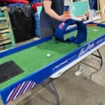 A person is playing mini-golf on a tabletop course decorated with Northwell and "The Park" branding at an indoor workshop, showcasing fun options like party rentals Long Island for unique gatherings and events.