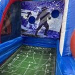 Inflatable football toss game with two holes on a backdrop of player silhouettes; the field-themed floor shows play diagrams and "TOUCHDOWN"—perfect for NY parties or bounce house Long Island party rentals.