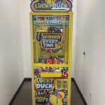 A yellow "Lucky Duck" claw machine, often seen at party rentals Long Island events, stands in a narrow hallway. Colorful signage reads “Winner Every Time!” and a cartoon duck is displayed on the front panel.