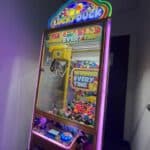 A brightly lit "Lucky Duck" claw machine filled with colorful plush toys stands in the corner of a dimly lit room, perfect for party rentals Long Island, NY. The display reads "Winner Every Time" above the glass case.
