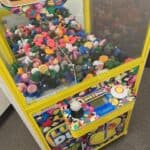 A claw machine filled with colorful rubber duck toys sits on a carpeted floor. The "Lucky Duck" machine, perfect for party rentals Long Island, features bright yellow and multicolored graphics that catch the eye.