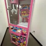 A brightly colored candy-themed claw machine game with pink trim, lollipop graphics, and a "Winner Every Time" sign stands in a party rentals Long Island showroom with white walls and a gray carpet.
