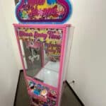 A colorful, pink "Sweet Shoppe" claw machine with candy-themed decorations, labeled "Winner Every Time," stands in a small hallway—perfect for party rentals Long Island, NY or pairing with a bounce house Long Island for sweet celebrations.