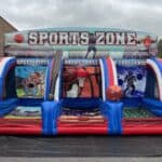 Inflatable “Sports Zone” game with sections for pitching, basketball, and football challenges—decorated with sports graphics and giant inflatable balls—perfect for outdoor fun from a bounce house Long Island party rentals company in NY.