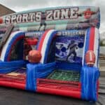 Inflatable sports game zone with three sections for baseball, basketball, and football challenges, decorated with large sports balls and action graphics, set up outdoors near a building—perfect for party rentals Long Island, NY.