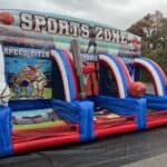 An inflatable sports-themed game structure with three sections labeled “Speed Pitch,” “Baseball,” and “Challenge,” featuring basketball hoops and large inflatable balls, perfect for party rentals Long Island, NY, set up outdoors on a black mat.