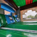 The photo features the interior of the MINECRAFT COMBO Bounce House, displaying shiny green, blue, and brown surfaces, large cushions, and a window with trees and a brick building visible outside.