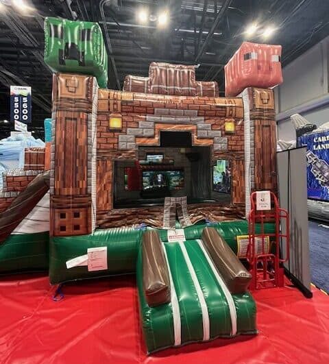 The MINECRAFT COMBO Bounce House, featuring blocky animal heads and video game-inspired design, sits on a red mat indoors—perfect for party rentals Long Island and adding fun to your next celebration.