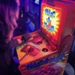 Two people play a brightly lit Whac-A-Mole arcade game in a dark room. Perfect for party rentals Long Island, one player is hitting the moles with a mallet while the other watches nearby.