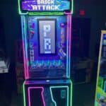 A brightly lit arcade game machine called "Brick Attack," with colorful neon lights and a digital display showing the word "PRIZE" in pixelated letters. Prize slots and controls are visible at the bottom—perfect for party rentals Long Island, NY.