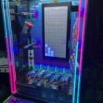 A neon-lit arcade prize machine, perfect for NY party rentals Long Island, features a Tetris-style game on a vertical screen with cans and snacks as prizes inside its transparent cabinet. Colorful controls and glowing lights surround the machine.