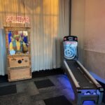 A Zoltar Speaks fortune-telling machine stands next to an arcade skee-ball game in a room with carpeted floor and curtains—perfect for party rentals Long Island or fun bounce house Long Island events.