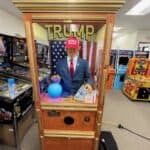 A fortune-telling arcade machine, popular at party rentals Long Island events, features a mannequin resembling Donald Trump in a red "Make America Great Again" hat and suit, with an American flag backdrop and "TRUMP" displayed above.