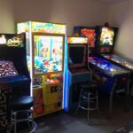 A small arcade room with a Pac-Man arcade machine, a claw crane game, Donkey Kong and Street Fighter II machines, a pinball machine, and two stools—perfect for party rentals Long Island or retro gaming fun in NY.