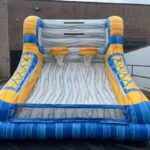 An inflatable basketball game with two hoops, designed to look like a basketball court in blue, yellow, and gray, set up outdoors near a brick building—perfect for party rentals Long Island or any NY event.