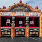 Three people sit inside a large inflatable slot machine, part of a bounce house Long Island setup. Each holds a sign with cherries as the “Jumbo Slot” display lights up. Bright signs and prize images pop in this outdoor NY party rentals scene.