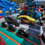 Two inflatable race cars, one black and one yellow, are positioned at a starting line inside a colorful bounce house Long Island race track with checkered flags and large inflatable decorations. Perfect for NY party rentals and racing fun!.