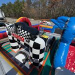 Inflatable racecar-themed obstacle course with checkered finish line arch and colorful, bouncy barriers, available through party rentals Long Island—set outdoors near parked vehicles and trees under a sunny NY sky.