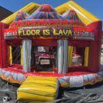A colorful inflatable bounce house designed to look like a volcano, available from party rentals Long Island. "FLOOR IS LAVA" is above the entrance, with lava graphics decorating the structure, set up outdoors on a black tarp.