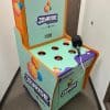 A colorful "Joyride" arcade machine, similar to whack-a-mole, stands in a hallway. It has a mallet attached by a cord and holes on top, with branding and logos, including “powered by Shopify.”.