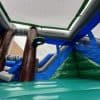 View from inside a large, colorful inflatable structure with blue, green, and brown sections, and netting overhead, partially outdoors near a brick building.