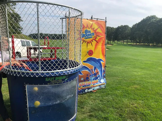 A blue dunk tank with a netted enclosure stands on grass near a colorful backdrop featuring dolphins and bubbles—perfect for your next event. Explore more party rentals Long Island options to make your celebration unforgettable.