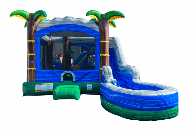 A blue and green inflatable bounce house with palm tree decorations and an attached curved slide, isolated on a white background.
