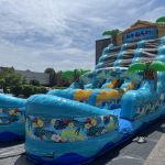 Large inflatable water slide with tropical decorations and "Beach Party" label set up outdoors on pavement.