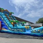 A colorful inflatable water slide with a beach theme is set up outdoors near a building on a sunny day.